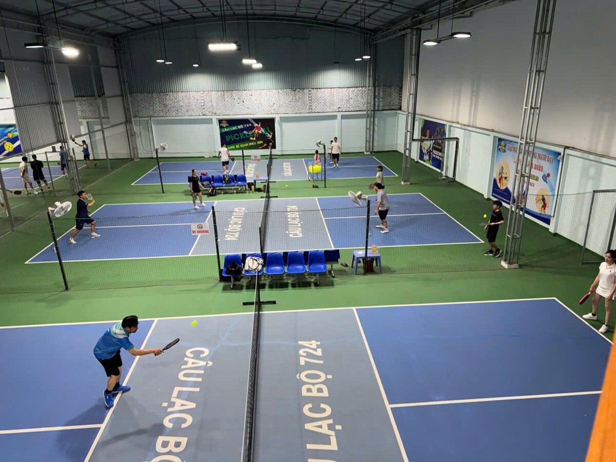 Toàn cảnh khu sân pickleball trong nhà của Câu lạc bộ 724 với bốn sân đấu, mặt sân xanh in chữ Câu lạc bộ 724, nhiều thành viên đang thi đấu dưới hệ đèn cao.