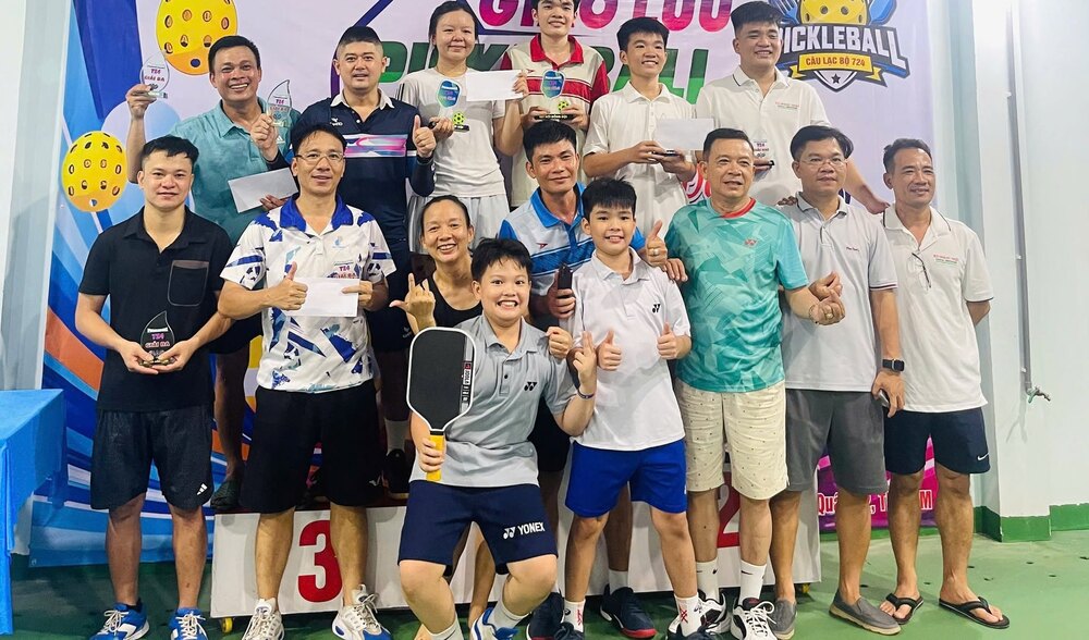 Các đội nhận cúp và phần thưởng trên bục trao giải của giải giao lưu Pickleball Câu lạc bộ 724, người lớn và các bạn nhỏ cùng chụp ảnh chung.